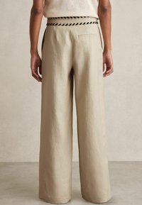 Beige wijde broek gemaakt van linnen, met een gestructureerde afwerking, contrasterende gevlochten tailleband en zijzakken.
