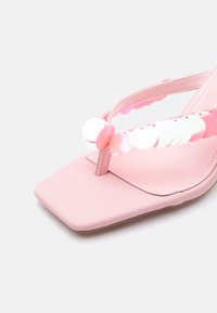 Ροζ σανδάλι με τετράγωνη μύτη και λουρί δαχτύλου διακοσμημένο με ιριδίζουσες στρογγυλές παγιέτες σε ανοιχτό φόντο.