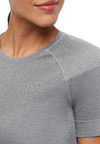 Szara sportowa koszulka z okrągłym dekoltem, krótkimi rękawami i teksturowanymi paskami na ramionach. Posiada subtelne logo.