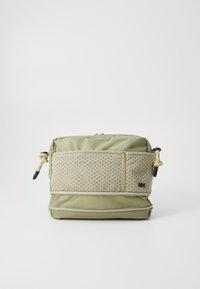 Borsa in tessuto verde con una tasca anteriore in rete beige testurizzata. Presenta chiusure a zip, una base rinforzata e dettagli in metallo nero.