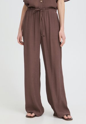 Persona che indossa pantaloni marroni larghi con coulisse abbinati a un top dello stesso colore e sandali neri con le dita dei piedi visibili.