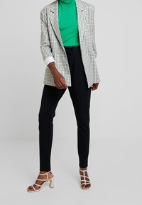 Controleer blazer in wit, groene coltrui, zwarte broek en beige blokhak sandalen; heeft een gestructureerd ontwerp, slanke pasvorm en contrasterende kleuren.