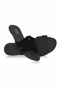 Czarne klapki wykonane z miękkiego zamszu, z dwoma nachodzącymi na siebie paskami, płaską gumową podeszwą i subtelnym złotym akcentem.