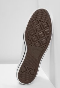 Braune Gummisohle mit Diamantprofil und „Converse All Star“-Markierung; weiße Seite mit schwarzem Akzentstreifen.