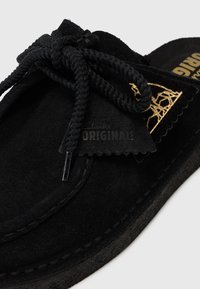 Chaussure noir en daim à enfiler avec un détail de lacet tressé, dotée d'une semelle intérieure texturée et d'un patch logo rehaussé d'or. Design à profil bas.