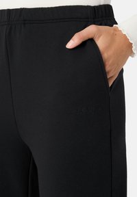 Sorte sweatpants med elastisk talje, sidelomme og diskret "LES LUNES" branding nær taljen. Blødt, struktureret stof.