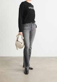 Schwarzer Pullover mit dem Text "HUG", graue ausgestellte Jeans mit fransigem Saum, schwarze spitze Ankle Boots und eine handbag in cremiger Farbe.