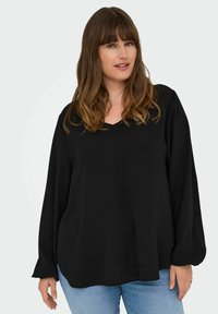 Crna majica dugih rukava s V-izrezom, izrađena od mekog materijala. Dizajn ima ležeran kroj i blago nabran rukav.