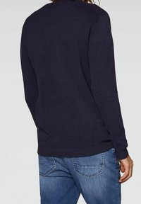 Maglione a maglia blu navy con finitura testurizzata, scollatura rotonda e polsini e orlo a costine, abbinato a jeans di denim azzurro.