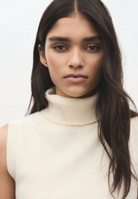 Pulover cu guler înalt, de culoare crem, cu accente striate, având o siluetă conică și design fără mâneci, așezat pe un fundal deschis.