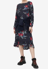 Marinblomstrad klänning med en stor rosett i midjan, volangkant och långa ärmar, matchad med svarta snörstövlar.