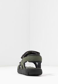 Sandalo verde dal design aperto, con suola testurizzata, cinturini in Velcro e dettagli neri a contrasto. Vista posteriore.
