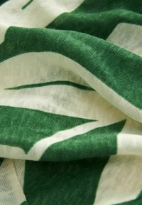 Tissu avec des motifs de feuilles vertes et blanches, montrant une texture douce et une forme fluide. Léger et superposé avec une apparence légèrement transparente.