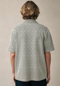 Camisa de manga corta con un patrón geométrico en blanco y negro, hecha de una tela texturizada con un corte relajado y un collar con muesca.