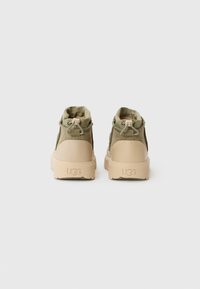 Gröna tygkängor i ankelhöjd med en flexibel krage, chunky beige sula och UGG-logotyp präglad på hälen.