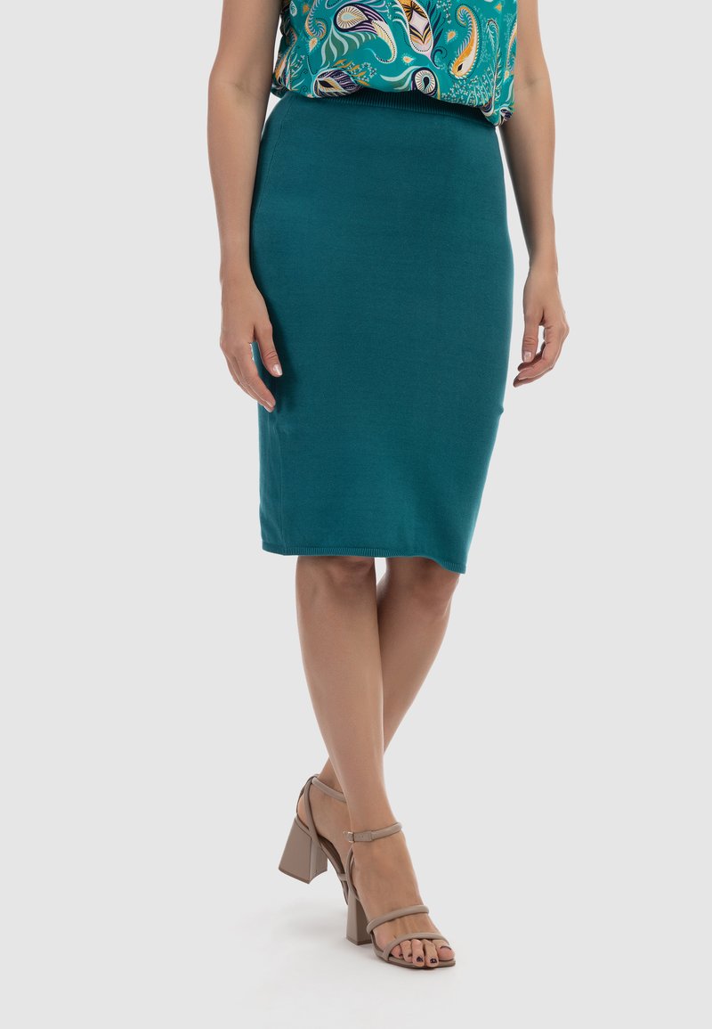 Fustă creion verde teal din material elastic, cu un design ajustat. Asortată cu sandale cu toc înalt, de culoare taupe, cu bretele.