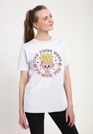 Kvinde i hvid T-shirt med tegneserie-pommes frites og hjerter, teksten lyder "Time fries when I'm with you,", ser op og smiler.