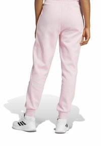 Ljusrosa sweatpants med avslappnad passform, elastisk midja och ribbade mudd. Bärs med vita sneakers med svarta ränder.