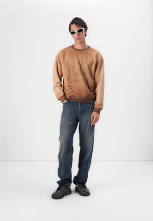 Brown sweatshirt with eagle graphic, light to dark gradient. Worn with blue jeans and black sneakers. Accessorized with white sunglasses.