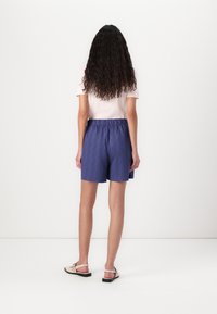 Blauwe textuurshorts met een elastische tailleband, gecombineerd met een lichtroze T-shirt en beige sandalen, weergegeven vanuit de achterkant.