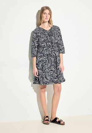 Abito con stampa paisley bianco e nero, vita cintrata, maniche a tre quarti e orlo a rouches. Indossato con sandali neri.
