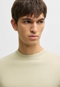 T-shirt a maniche corte, aderente, in tessuto a coste beige chiaro con scollo rotondo. Texture liscia, design minimal, adatta per essere indossata a strati.