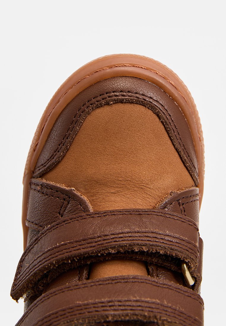 Bruine leren schoen met klittenbandsluitingen; heeft een gladde bovenkant en textuuraccenten. Ronde neus en een contrasterende zool in een lichtere tint.