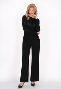 Pulover negru tricotat cu un model în zigzag, asortat cu pantaloni largi cu talie înaltă negri și balerini negri cu vârf ascuțit.