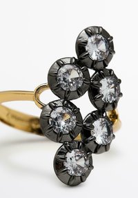 Bague en métal noir ornée de six gemmes rondes claires disposées en un motif floral, avec une bande lisse en or et une finition polie.