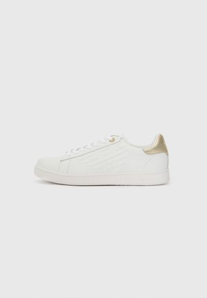 White sneaker made of leather with a smooth finish. Features a gold accent on the heel and logo detailing on the side. Laced front design.