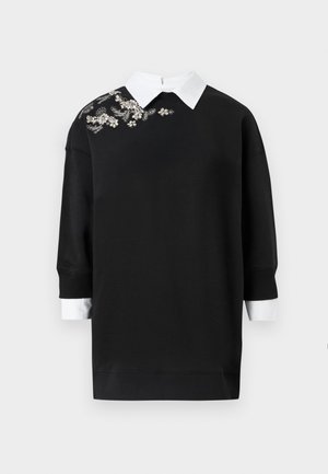 Juodas megztinis su balta apykakle, puoštas dekoratyvine gėlių siuvinėjimu ant kairio peties. Ilgos rankovės ir gipiūro uždangalai.