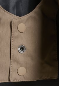 Gilet beige con motivo a spina di pesce, dotato di due bottoni marroni e un bottone a pressione decorativo argentato sul davanti.