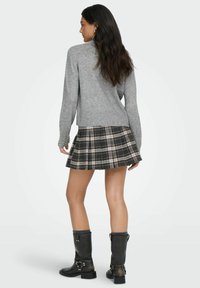 Grå strikkegenser med perle detaljer på ermene, sammen med et rutete plissert skjørt i mørke toner. Sorte ankelstøvler med spenner fullfører antrekket.