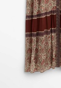 Robe maxi en tissu léger, présentant une base crème avec des motifs floraux rouges, des sections bordeaux et des bordures délicates. Détails de boutons présents.