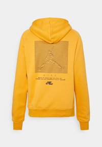 Sudadera de algodón amarilla con cordón, que presenta un diseño gráfico de líneas y picos en la parte posterior, junto con detalles de marca en negro.