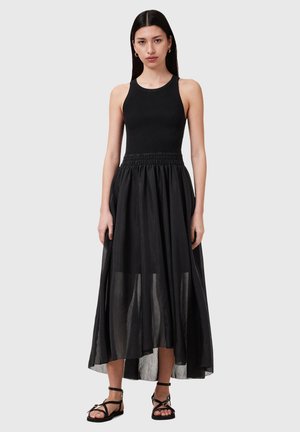 Zwarte jurk met een aansluitende geribbelde top en een vloeiende, doorschijnende gelaagde rok. Heeft een smocktail en een enkel-langere zoom. Gedragen met strap sandalen in het zwart.