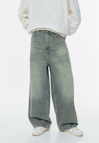 Blugi evazați din denim gri deschis cu un finisaj decolorat, având talie înaltă și detalii de cusătură pronunțate. Asortați cu adidași albi.