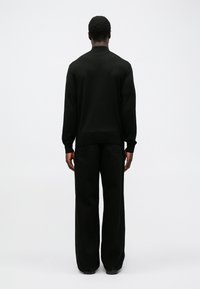 Pulover negru tricotat cu guler rotund, combinat cu pantaloni negri cu picioare largi. Textură netedă; design minimalist, fără modele sau accente vizibile.