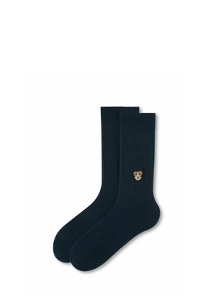 Paire de chaussettes noires montantes avec un petit détail brodé d'un visage de chien près de la cheville sur une chaussette, présentée sur fond blanc.
