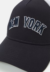 Navy blue baseball cap with "NEW YORK" embroidered in white and dark blue, featuring a textured crown and stitched visor.