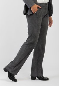 Pantaloni in velluto grigio con design a gamba dritta, dotati di tasche frontali e una texture liscia, abbinati a stivali neri con tacco.