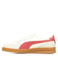 Sneakers bianchi in pelle con una striscia rosa e dettagli perforati, dotati di una suola in gomma marrone e un design tradizionale con lacci.