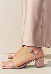 Sandali con tacco rosa chiaro, punta quadrata, finitura opaca e cinturino regolabile alla caviglia. Tacco spesso che offre stabilità e supporto.