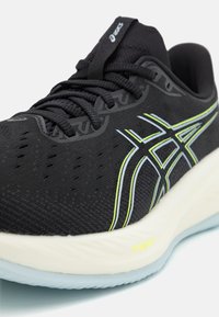 Zapatilla deportiva negra con parte superior de malla transpirable, líneas de acento en verde y azul, y una suela gruesa blanca con la marca FF Blast+.