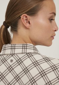 Hemdkragenhemd mit einer cremefarbenen Grundlage und braunem Karomuster. Texturierter Stoff mit einem kleinen Logo auf der Rückseite, das ein ordentliches, maßgeschneidertes Design zeigt.
