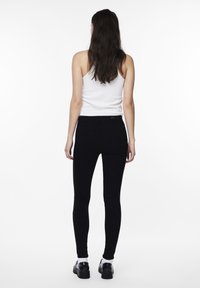 Black skinny jeans made of denim, featuring a high waist, smooth texture, and back pockets. Paired with a white tank top and black shoes.