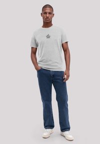 Gray cotton t-shirt with short sleeves, featuring a black graphic design at the chest. Paired with blue denim jeans and white sneakers.