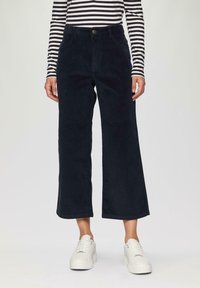Donker marineblauwe corduroy cropped broek met een rechte pijp en voorzakken, gecombineerd met witte platform sneakers en een gestreept lange mouwen shirt.