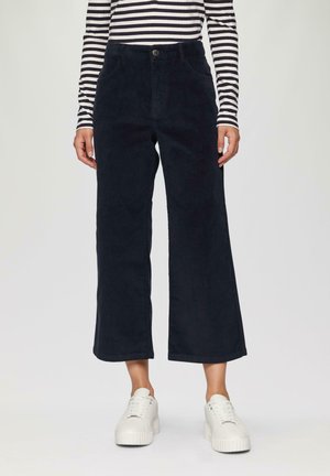 Pantalons en velours côtelé bleu marine foncé, cropped, avec une jambe droite et des poches avant, associés à des baskets blanches à plateforme et un haut rayé à manches longues.