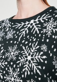Maglione verde con un motivo a fiocchi di neve bianchi, un collo rotondo e un tessuto a maglia testurizzato. Adatto per l'abbigliamento invernale.